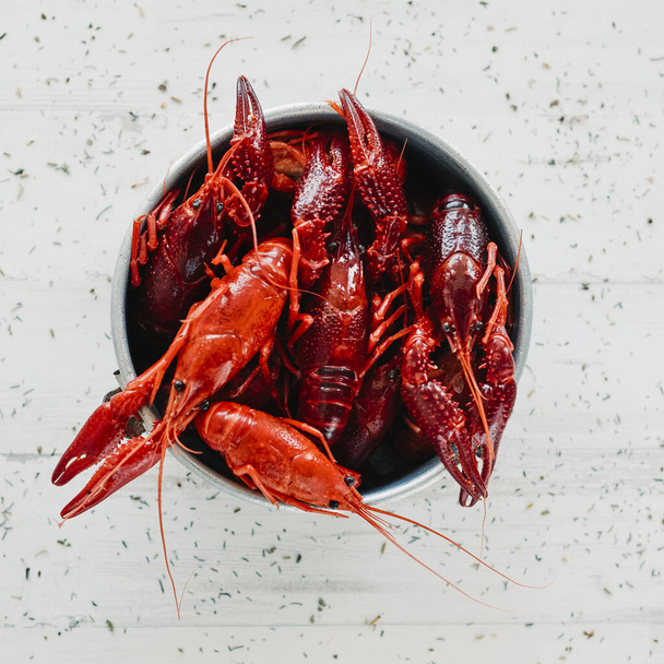 high angle view of some cooked crayfishes in an old metal container, on a white surface sprinkled with different culinary herbs - Фото, изображение