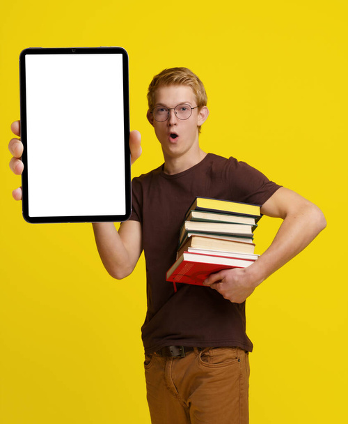 Surprised student holding books and a Tablet PC with a blank white screen for copy space against a yellow background, showcasing the concept of modern education and the integration of technology in - Fotoğraf, Görsel