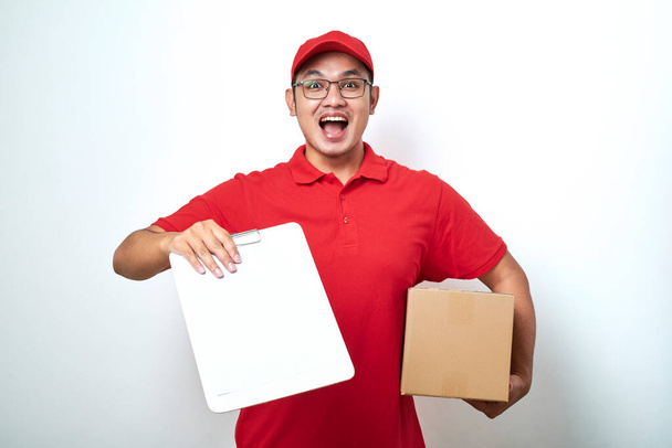 Asian delivery man or courier wearing red uniform showing blank clipboard asking for signature , standing over white background - Photo, Image