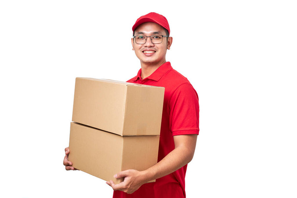  Asyalı genç kurye kırmızı şapkalı ve tişörtlü, izole edilmiş beyaz arka planda duruyor. Önünde karton kutular var. - Fotoğraf, Görsel