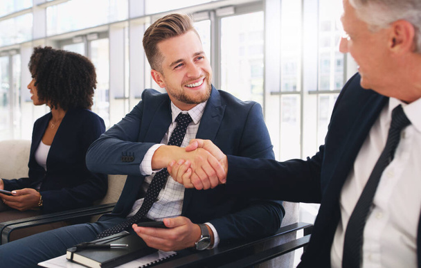 Hello Its a pleasure to meet you. Cropped shot of a handsome young businessman shaking hands with a colleague while sitting in a line in the office - Foto, Imagen