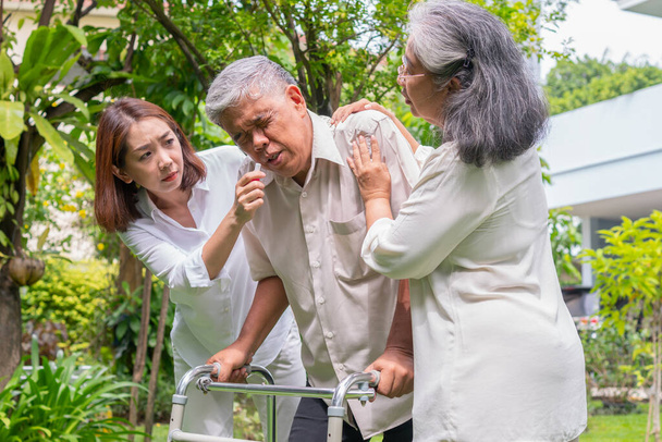 Yaşlı, mutlu Asyalı bir adam yürüteç kullanıyor ve onunla birlikte bahçede yürüyor. Hemşire ve karısı. Bakıcının, birikimin ve sağlık sigortasının özenle mutlu emeklilik kavramı - Fotoğraf, Görsel