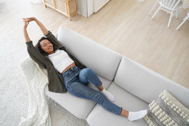 Young woman lying on comfy sofa. Smiling girl stretching body awaking after sleep on cozy couch breath fresh air inside modern living room, enjoying leisure, break, weekend. Recreation, stress relief. - Photo, Image