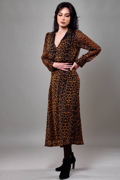 Beautiful portrait of a brunette woman wearing an animal print dress. - Фото, изображение
