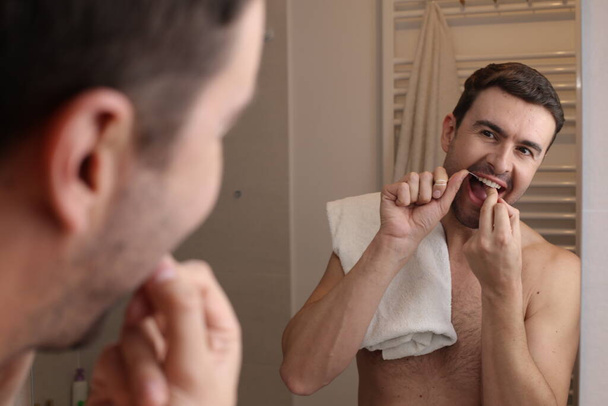 portret przystojnego młodzieńca używającego nici dentystycznej przed lustrem w łazience - Zdjęcie, obraz