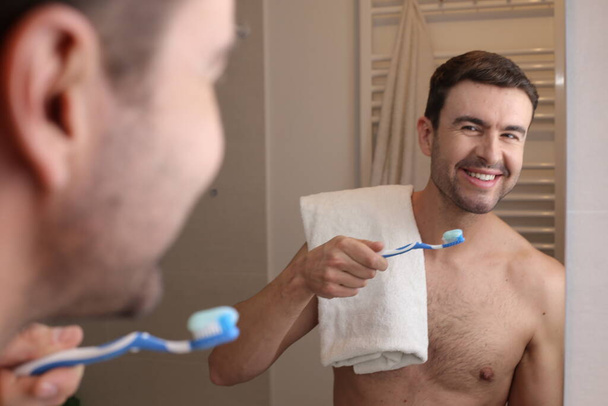 портрет красивого молодого чоловіка чистить зуби перед дзеркалом у ванній
 - Фото, зображення