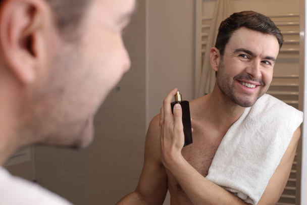 portret van knappe jonge man van toepassing parfum in de voorkant van de spiegel in de badkamer - Foto, afbeelding