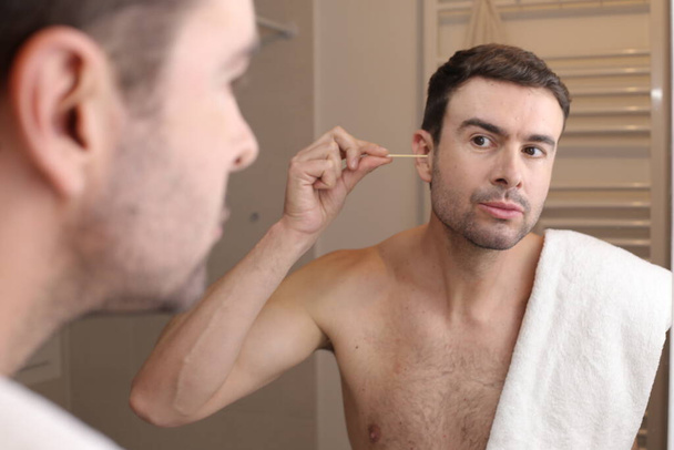 portré jóképű fiatalember takarítás fülek pamut pálca előtt tükör a fürdőszobában - Fotó, kép