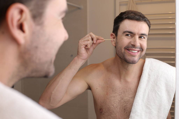 ハンサムな若い男の肖像画バスルームの鏡の前に綿棒で耳を掃除 - 写真・画像