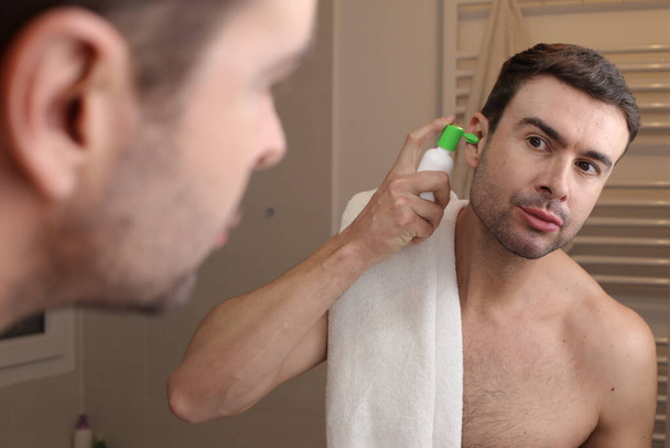 Porträt eines hübschen jungen Mannes, der vor dem Spiegel im Badezimmer Hygienespray für die Ohren benutzt - Foto, Bild