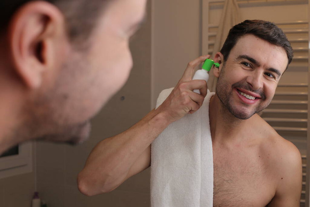 portré jóképű fiatalember használ higiéniai spray füle előtt tükör a fürdőszobában - Fotó, kép