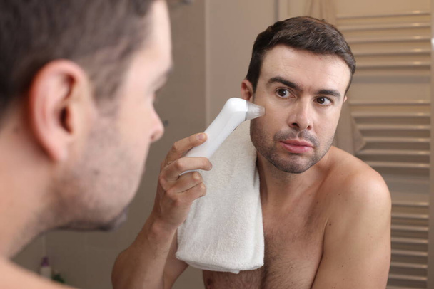 portrait of handsome young man using vacuum pimple remover in front of mirror in bathroom - Photo, Image
