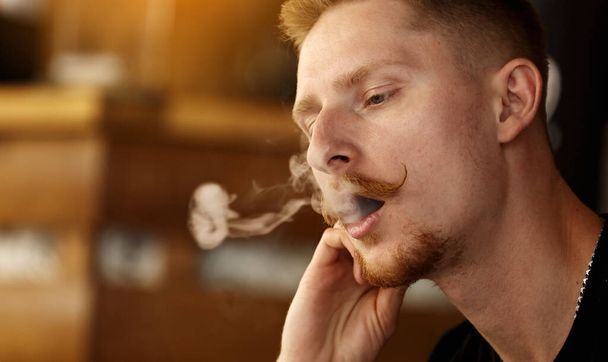 handsome young man with beard and mustache Vaping an Electronic Cigarette. hipster guy Exhaling Smoke Rings - Photo, Image