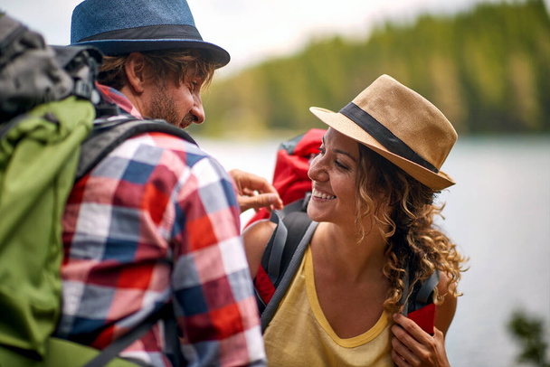 close up of young adult couple in nature, looking each other, smiling, with backpacks and hats. healthy lifestyl - Fotó, kép
