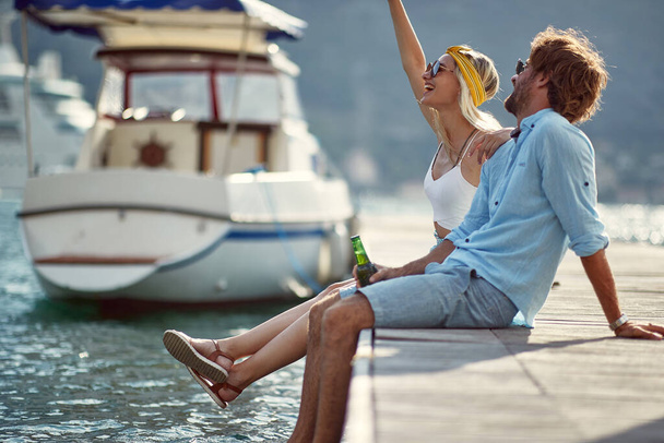 adult caucasian couple sitting on a dock, talking, smiling, laughing, enjoying at the seaside by the boat - Foto, Imagem
