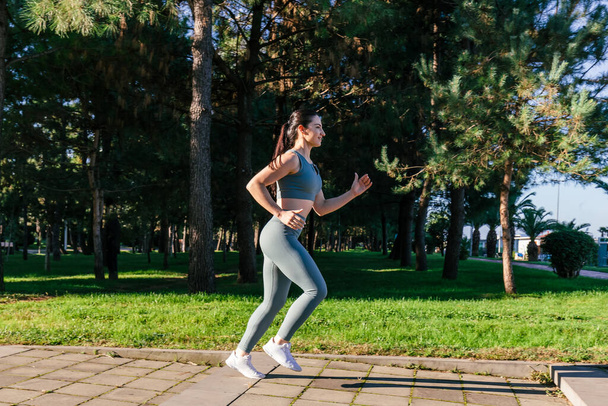 Sportif ve güler yüzlü genç bayan spor giyim koçu parkta koşuyor. Spor açık hava konsepti. - Fotoğraf, Görsel