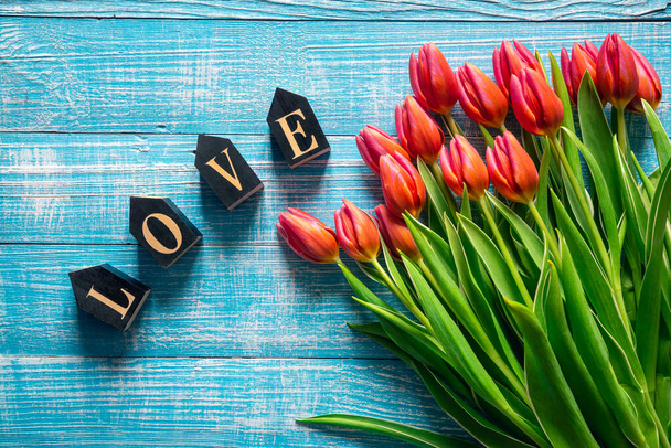 Bouquet of pink tulips and decorative word love on a blue wooden background, top view. - 写真・画像