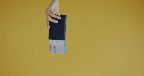 Close-up of female hand holding document and tickets and playing with toy plane on yellow color background. Tourism destination and transport concept. - Photo, image