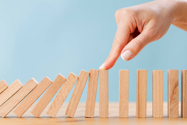 Business woman's finger try to stopping falling wooden dominoes blocks for business solution concept. Business crisis effect or risk protection concept - Φωτογραφία, εικόνα