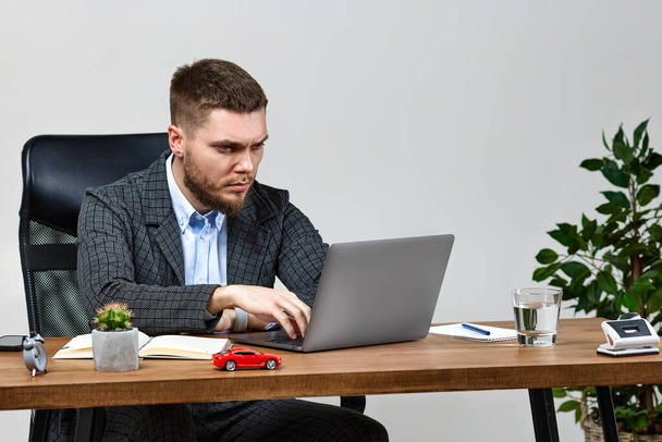 young bearded businessman typing on computer keyboard, sending emails to business partners, sitting on chair at desk - Fotó, kép