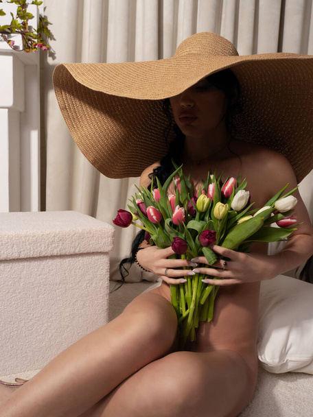 Schöne sexy stilvolle nackte Frau mit einem schönen Strauß Tulpen in einem riesigen Strohhut - Foto, Bild