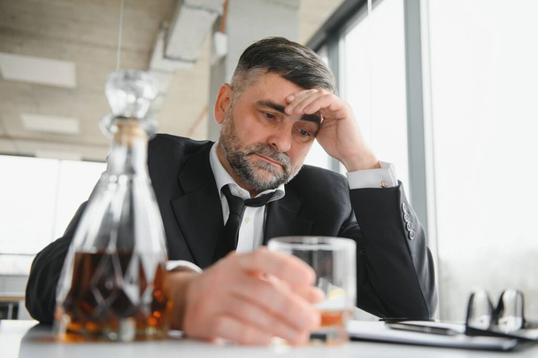 Old male employee drinking alcohol at workplace. - Фото, изображение