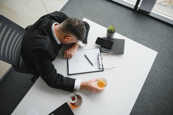 Close up of stressed businessman holding a glass of whiskey he sleeping and Data Charts,business document at office desk. alcohol addiction and drunk businessman concept. - Foto, immagini