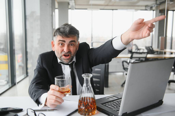 Old business man is drinking alchool at the office. - Фото, зображення