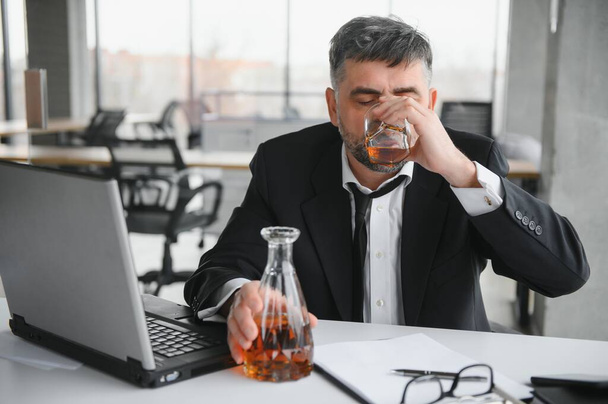 Old male employee drinking alcohol at workplace. - Φωτογραφία, εικόνα