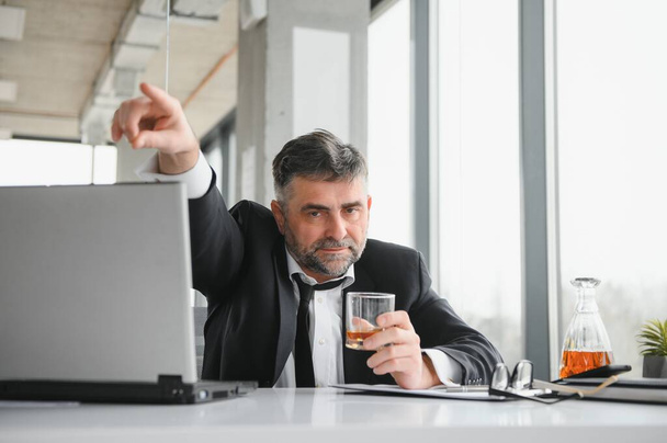 Old business man is drinking alchool at the office. - Фото, зображення