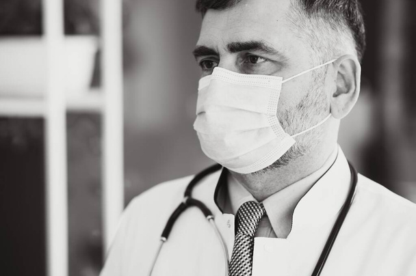 Mature old medical healthcare professional doctor wearing white coat, stethoscope, glasses and face mask standing in hospital. Medical staff health care protection concept. Portrait. - Foto, imagen