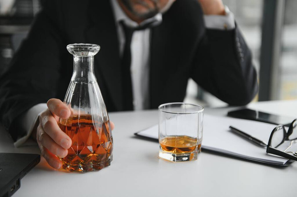 Old male employee drinking alcohol at workplace. - Photo, image