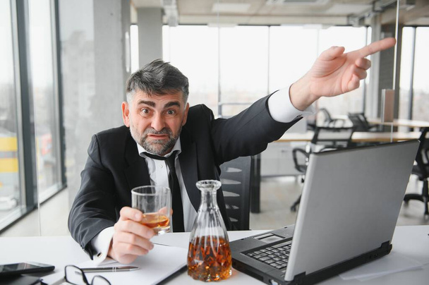 Old male employee drinking alcohol at workplace. - Fotoğraf, Görsel