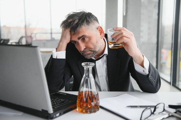 Old male employee drinking alcohol at workplace. - Foto, immagini