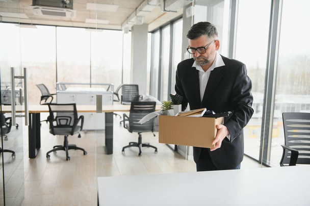 Portrait of sad dismissed senior old business man worker taking his office supplies in the box. Pensioner mature retire from work carry staff back home. Lifestyle business retirement, quit job concept. - 写真・画像