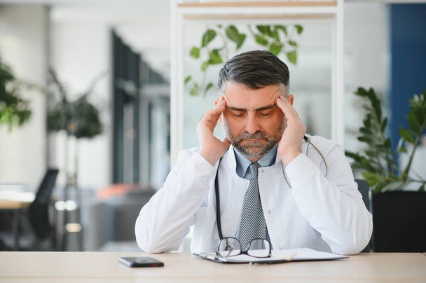 Mature doctor man at the clinic tired rubbing nose and eyes feeling fatigue and headache. stress and frustration concept - Photo, Image
