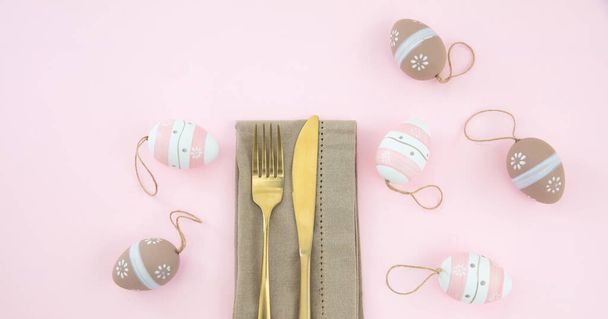 Налаштування великодніх столів, прикраси великодніх яєць, серветки та золоті столові прибори на пастельно-рожевому тлі, вид зверху
 - Фото, зображення