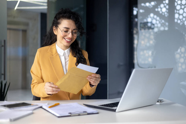 Successful hispanic woman inside office at work businesswoman received postal envelope letter notification with good news, female worker celebrating victory and good results achievement at workplace. - Foto, immagini