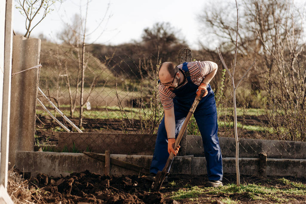 O jardineiro está cavando o jardim com uma pá. Retrato de um homem trabalhando em seu jardim em um belo dia de primavera. - Foto, Imagem