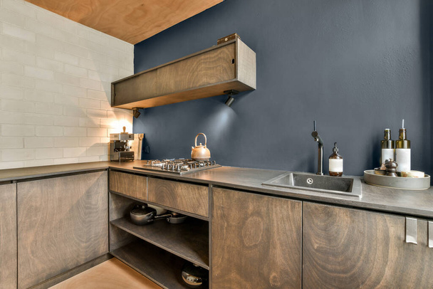 カウンターの上に青い壁と木製の食器棚を備えたモダンなキッチンはワインラックとしても使用されています - 写真・画像