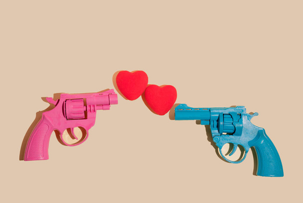 Creative valentines or romantic concept with pink and blue gun firing hearts on  yellow background. Minimal love concept. - Foto, afbeelding