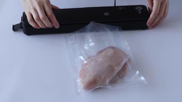 Mujer pone bolsa de vacío de pechuga de pollo en la máquina de vacío en la mesa blanca. - Metraje, vídeo
