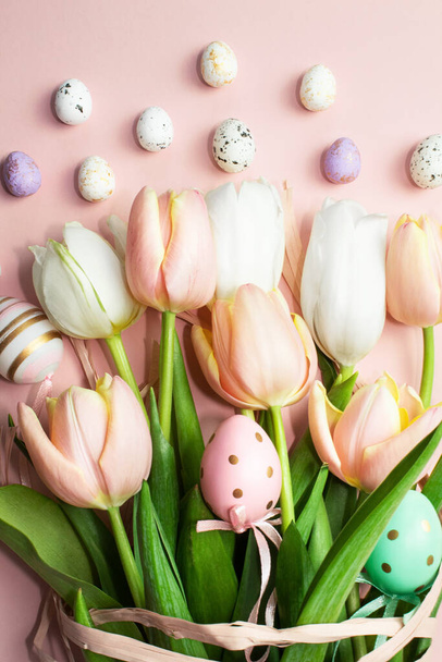 Composición vertical de Pascua de tulipanes rosados y blancos, cinta, huevos decorativos sobre un fondo rosado. Ramo de tulipanes, flores de primavera. Contenido para vacaciones de Pascua. Plano, vista superior, primer plano, espacio para copiar - Foto, imagen