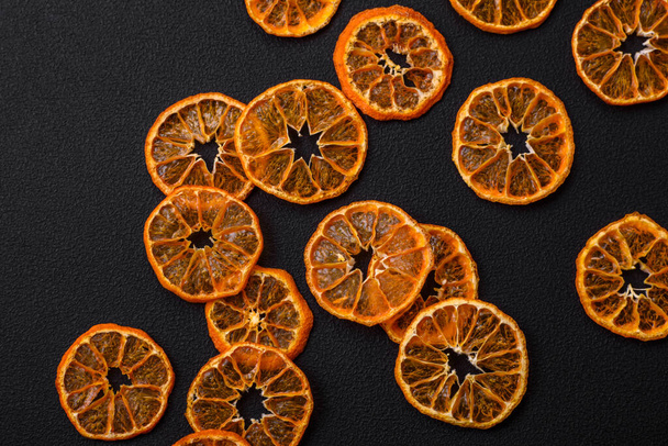 Dried round shape slices of bright orange color tangerine on a dark textural background - Фото, изображение