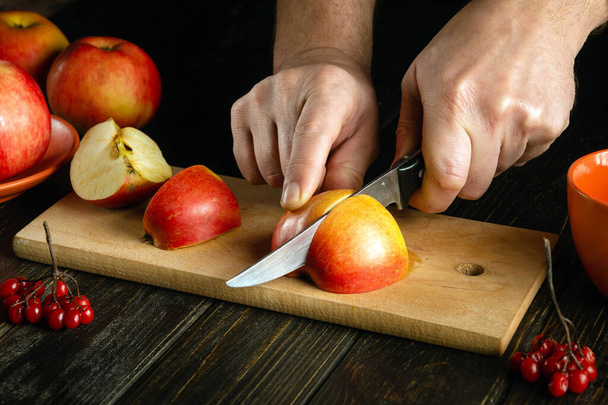 Cook's hands with a knife cut apple on a cutting board to make compote or fruit juice. Apples diet for a set of vitamins. Work environment on the kitchen table - Fotó, kép