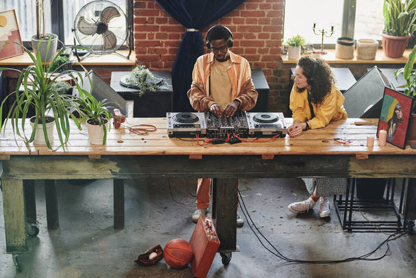 joven interracial pareja en auriculares y casualwear crear nuevo música mientras negro hombre ajuste sonidos en dj controlador - Foto, imagen