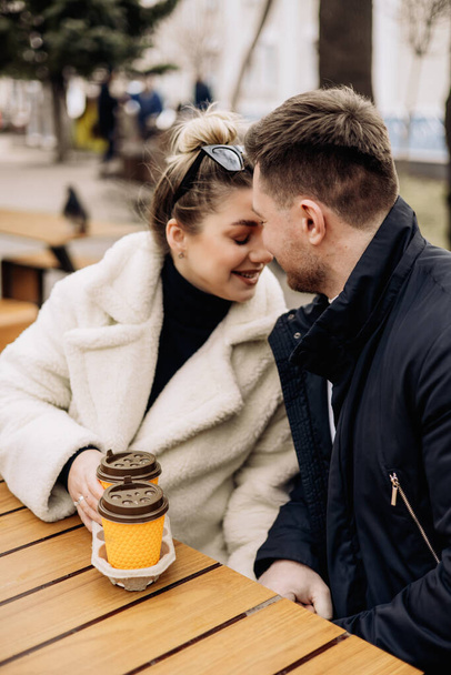 Glückliches junges verliebtes Paar in Oberbekleidung, das draußen an einem Tisch sitzt und Kaffee trinkt. Entspannen an der frischen Luft - Foto, Bild