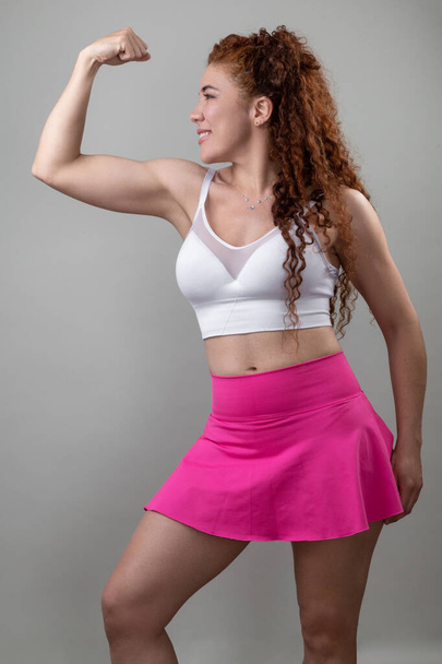 мышечная рука молодой женщины с вьющимися волосами, носит спортивную одежду, природную красоту латинской модели, оздоровление с упражнениями, здоровый образ жизни - Фото, изображение