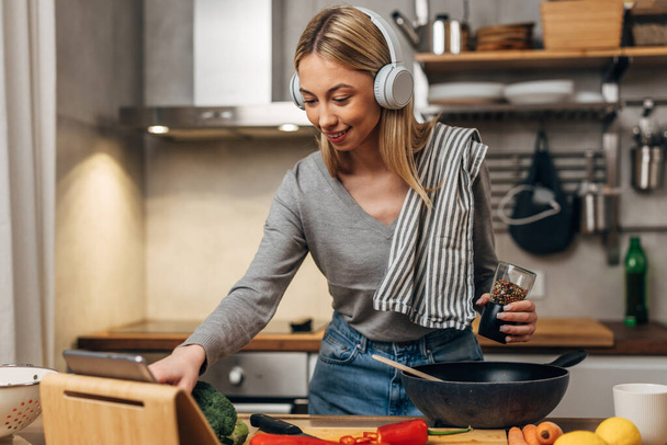 Happy woman cooks in the kitchen and listens to music - Foto, afbeelding