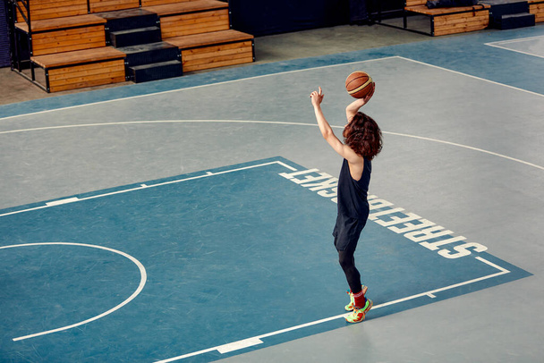 Спортивный парень на баскетбольной площадке, парень с длинными волосами тренируется с мячом на баскетбольной площадке, стритбол - Фото, изображение